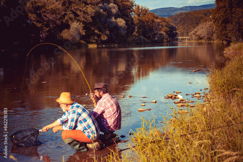 Принти на полотні Young and old fisherman standing on the shore of lake with fishing rod
