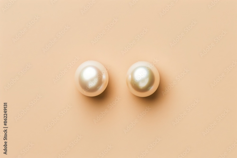 Minimalist photograph of two simple, elegant, off-white pearl earrings on a soft peach background. Minimalist photograph of two simple, elegant, off-white pearl earrings on a soft peach background.