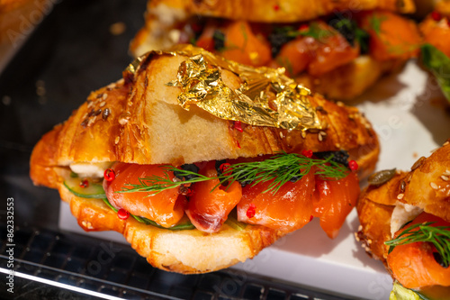 Butter puff croissants on display in artisanal bakery in London, filled with Scottish smoked wild salmon fish and caviar, decorated with real 24 carat gold foil photo