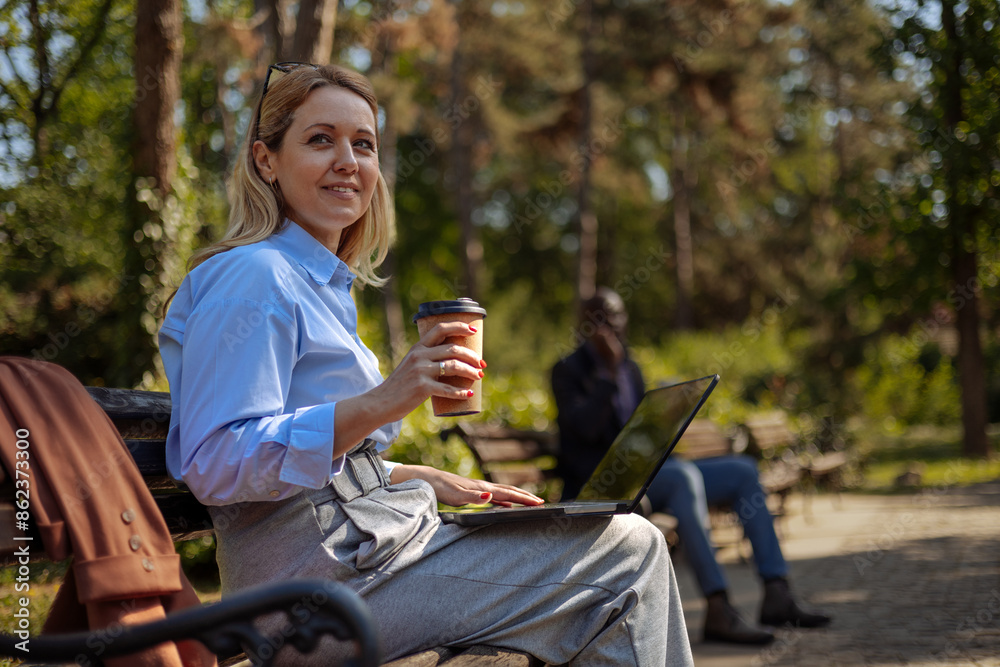 Fototapeta premium Woman sitting on a park bench, working on her laptop