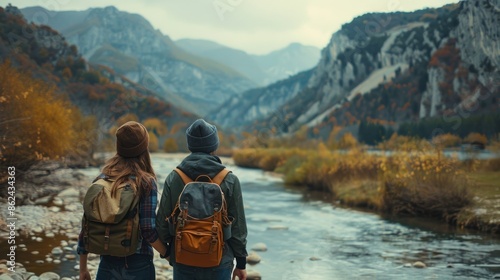 A view of a young man and woman holding a backpack while walking and admiring the scenery of mountains and rivers in front of them. Holiday