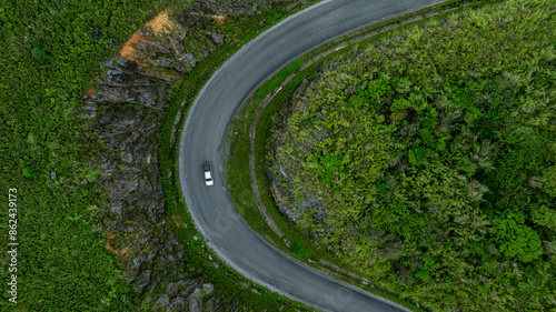 Aerial view road through the green forest on mountain road, Car drive on asphalt road going through green forest, Curved road from above.