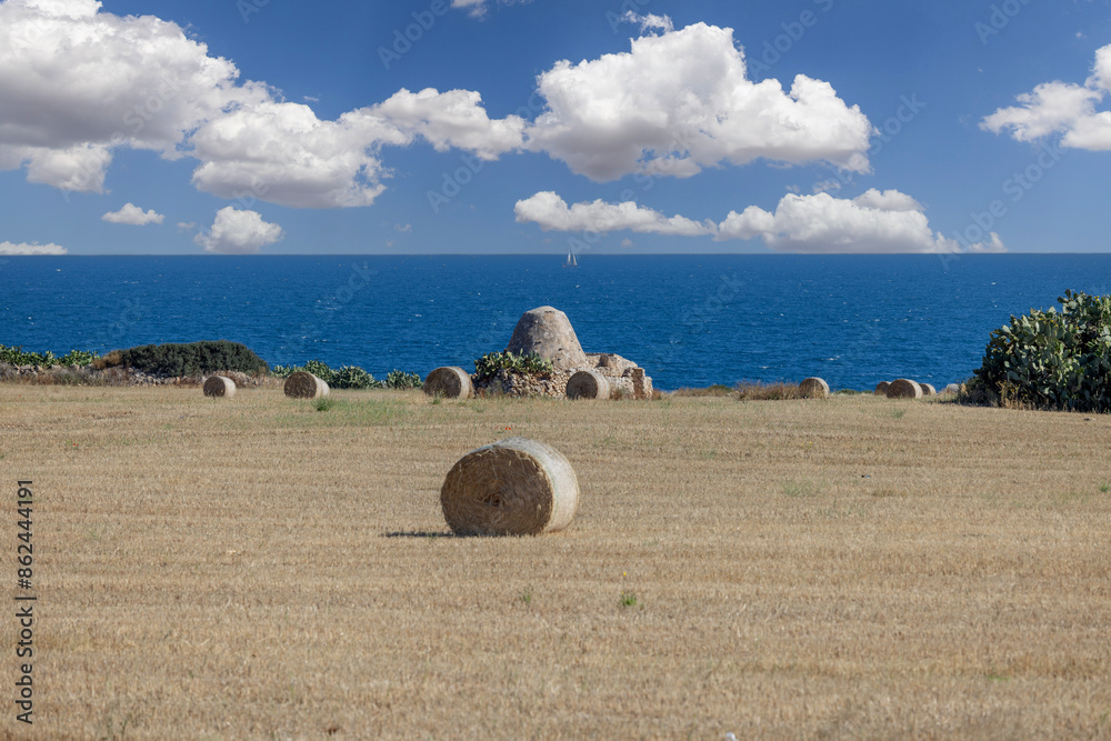 Picturesque view of the farm field after harvest, large straw bales and old trullo cottage on the coast of Adriatic Sea, Italy, Apulia