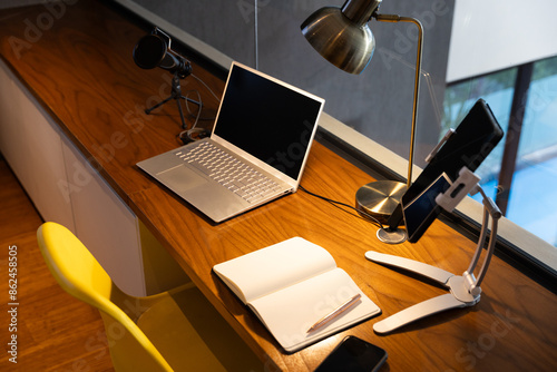 Home office setup with laptop, microphone, notebook, and tablet on wooden desk, copy space photo