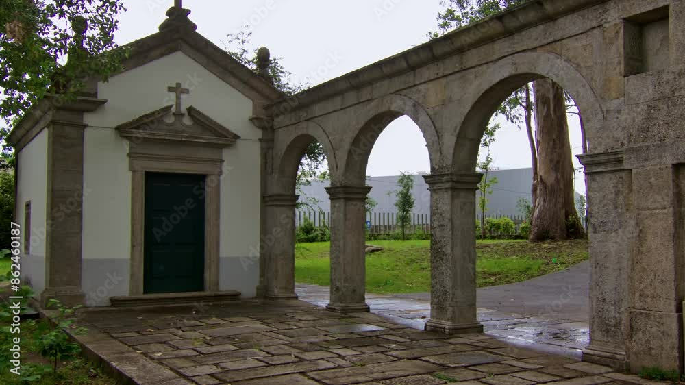A static shot of a little christian chapel in a park in Porto. With a little stone arch construction next to it.