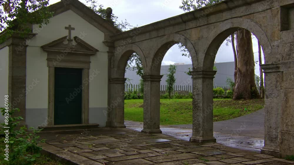 Static shot of a little christian chapel in a park with some stone arches by, in Porto.