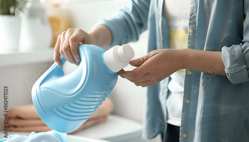 Woman pouring fabric softener from bottle into cap for washing clothes indoors, closeup. Space for text photo