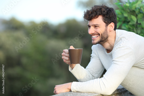 Happy man in a terrace drinking coffee looking away
