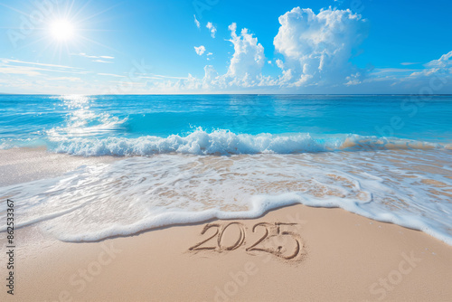 The year 2025 written in the sand as waves gently wash ashore under a bright sun.