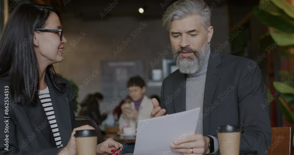 Mature man and young woman business partners talking pointing at document and doing high-five hand gesture in cafe. Successful collaboration and businesspeople concept. Mature man and young woman business partners talking pointing at document and doing high-five hand gesture in cafe. Successful collaboration and businesspeople concept.