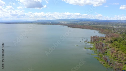 Lake Naivasha picturesque cinematic aerial view. Vast water surface, lush greenery, and a clear blue sky with scattered clouds, offering a serene and scenic landscape of Africa