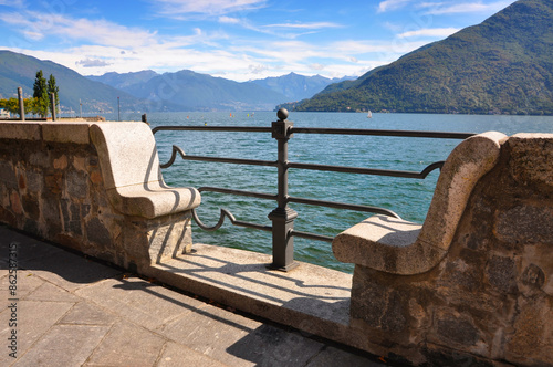 Wall Bench on the Waterfront to Lake Maggiore with Mountain and Blue Sky with Clouds in a Sunny Day in Cannobio, Piedmont, Italy. photo