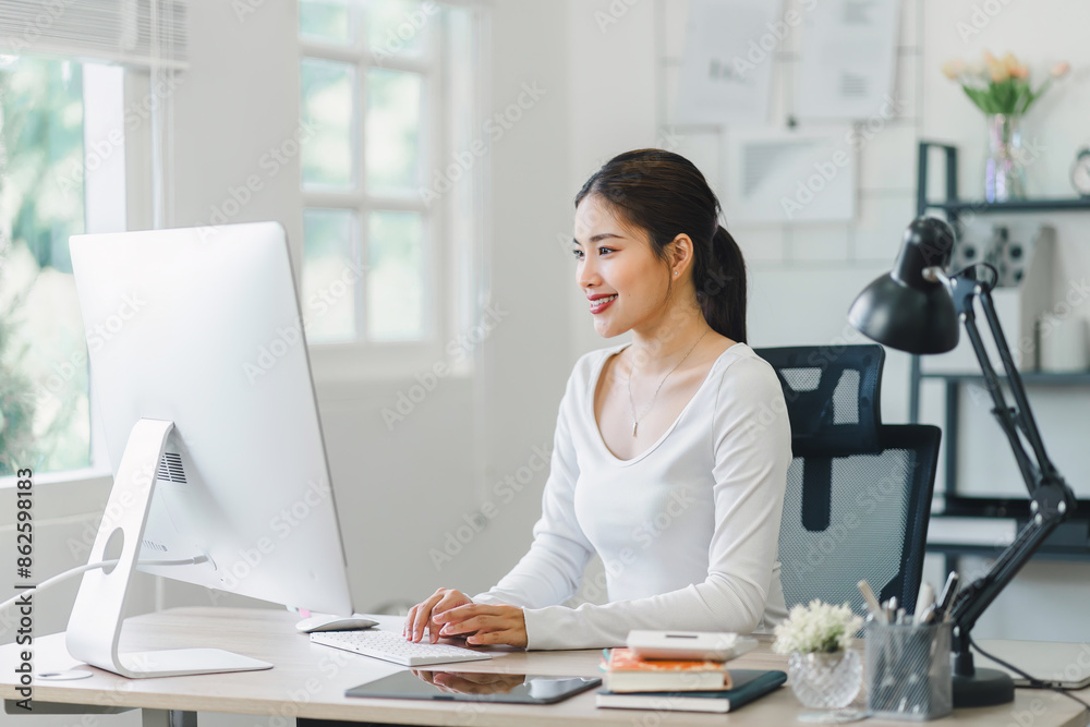 Smiling woman working on desktop while sitting in comfortable home office with notebook and documents. Smiling woman working on desktop while sitting in comfortable home office with notebook and documents.