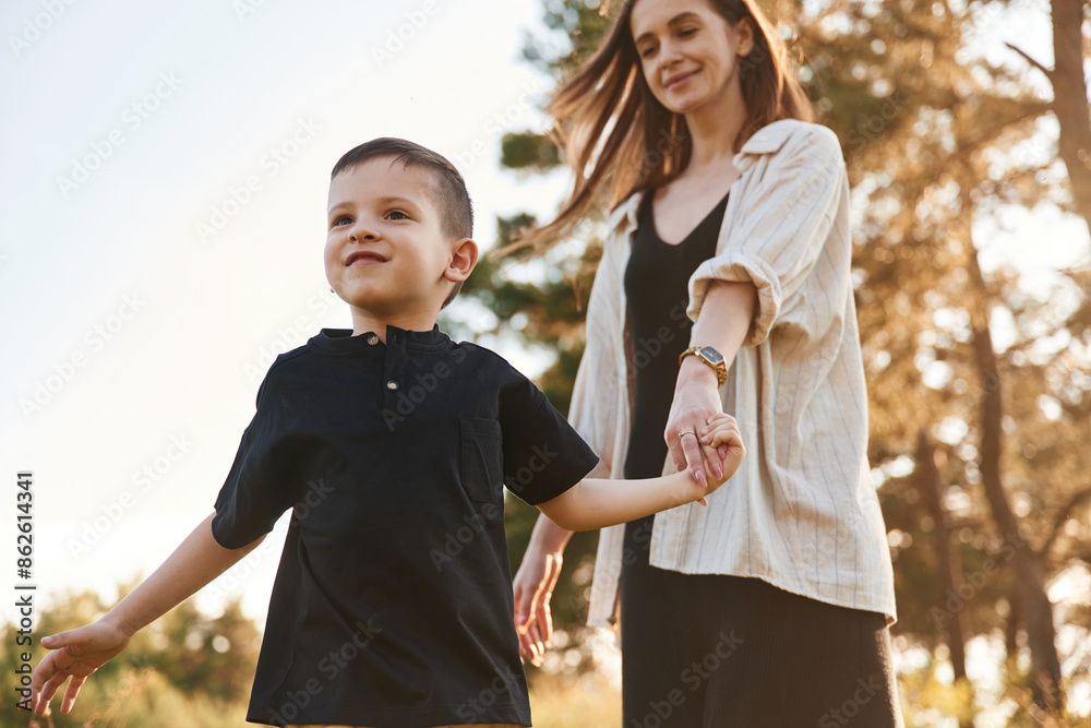 Fototapeta premium Holding each other by a hands. Mother and son are in the forest together