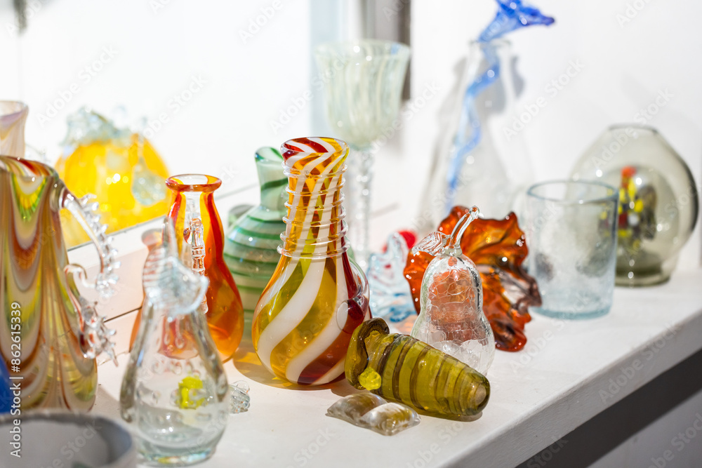 Colorful craft glasses and vases are on a windowsill, close-up Colorful craft glasses and vases are on a windowsill, close-up