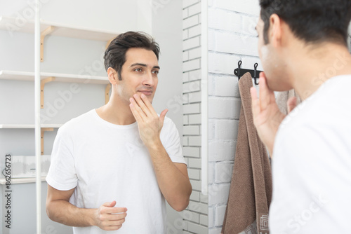 Bilde på lerret Handsome man looking at mirror and applying moisturizing cream on cheeks in bathroom