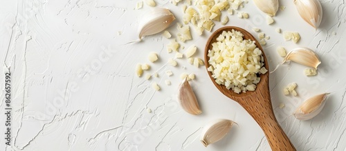Wooden ladle with minced garlic on a white desk with a plain background, presenting a top view of the copy space image.