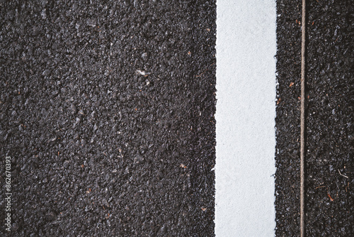 Close-up of a freshly painted white line on a black asphalt road, highlighting the texture and contrast between the two surfaces.