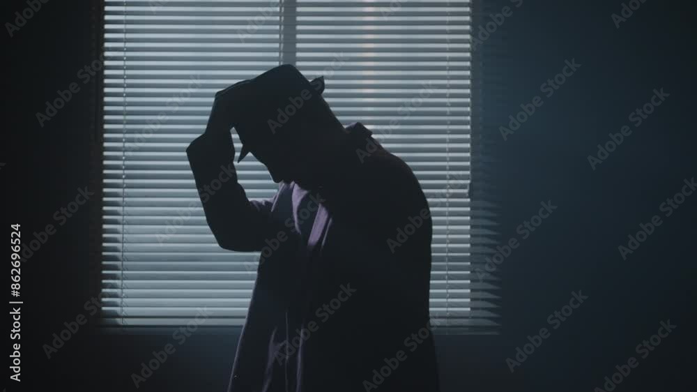 Noir spy film character puts hat on in a dark room next to the window backlight. High quality 4k footage