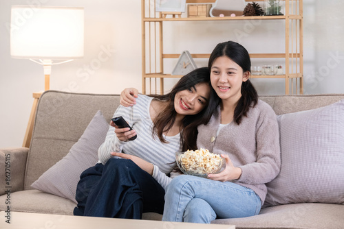 LGBT Lesbian Couple Enjoying Leisure Time Together on Couch with Popcorn and Remote Control in Cozy Living Room photo