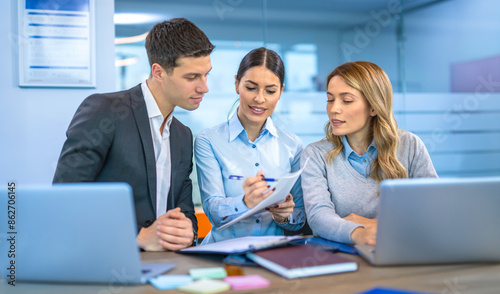 Two female colleagues and handsome male business associate analyzing a business document together in modern office.