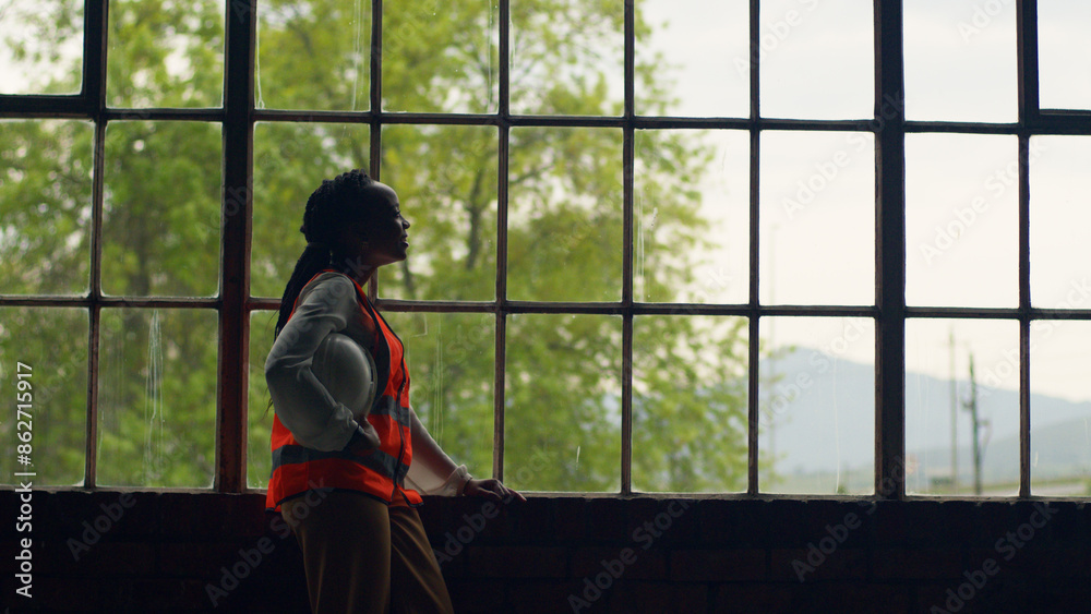 Female Engineer Reflecting By Window In Construction Setting With Safety Gear Female Engineer Reflecting By Window In Construction Setting With Safety Gear