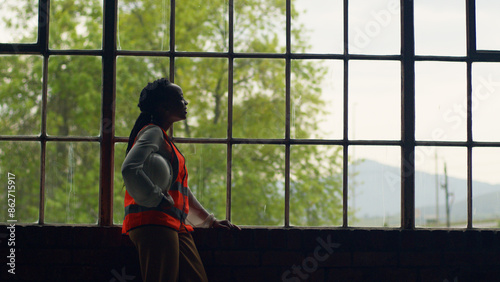 Female Engineer Reflecting By Window In Construction Setting With Safety Gear