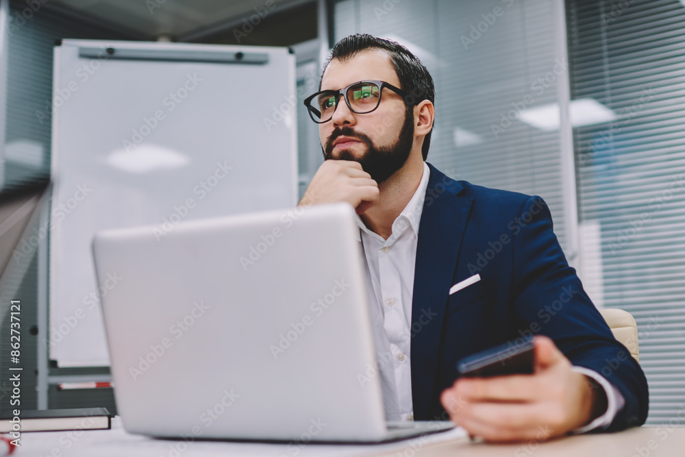 Thoughtful businessman dressed in suit thinking on productive strategy for developing own financial company working at modern laptop computer connected to wireless 4G internet in stylish office Thoughtful businessman dressed in suit thinking on productive strategy for developing own financial company working at modern laptop computer connected to wireless 4G internet in stylish office