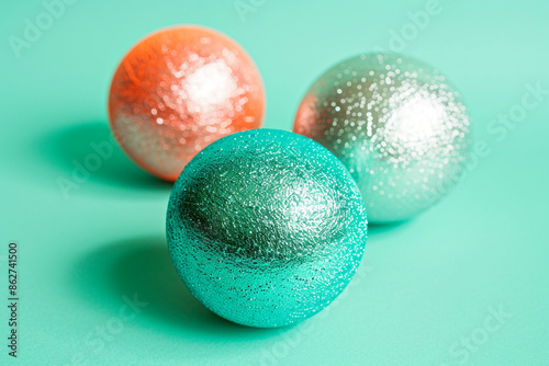 Three radiant teal, silver, and coral orange balls with slightly textured finishes on a solid, clean mint green background.