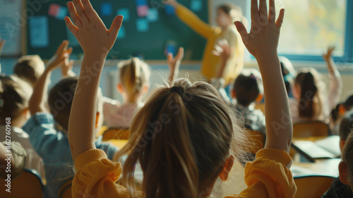 A view from behind of schoolchildren raising their hands in a school classroom against the background of a teacher