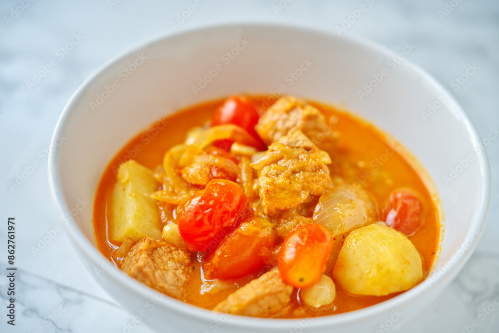 The traditional Thai curry called Pork Masaman curry, the masaman curry is in white bowl on marble table. Close up Thai food image. The traditional Thai curry called Pork Masaman curry, the masaman curry is in white bowl on marble table. Close up Thai food image.