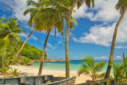 Fototapeta Naklejka Na Ścianę i Meble -  Docked fisherman's boat on the sand under coconut palm trees near the beach of Anse Takamaka, sunny day with blue sky and white sandy beach, turquoise water, Mahe Seychelles