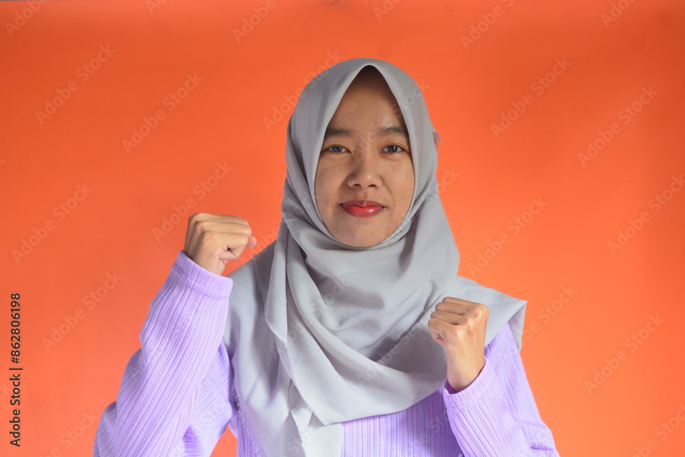 Portrait of an Asian Muslim woman with an enthusiastic and powerful boxing stance, isolated on an orange background Portrait of an Asian Muslim woman with an enthusiastic and powerful boxing stance, isolated on an orange background
