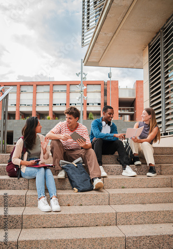 Canvastavla Vertical multiracial group of students sitting on the university campus staircase, talking and studying a lesson on a tablet