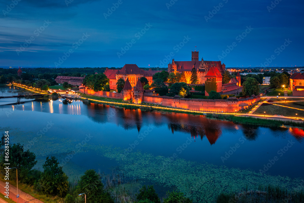 Fototapeta premium Castle of theTeutonic Order in Malbork by the Nogat river at dusk.