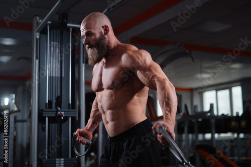 Bald Caucasian bodybuilder training chest using cable crossover in gym. 