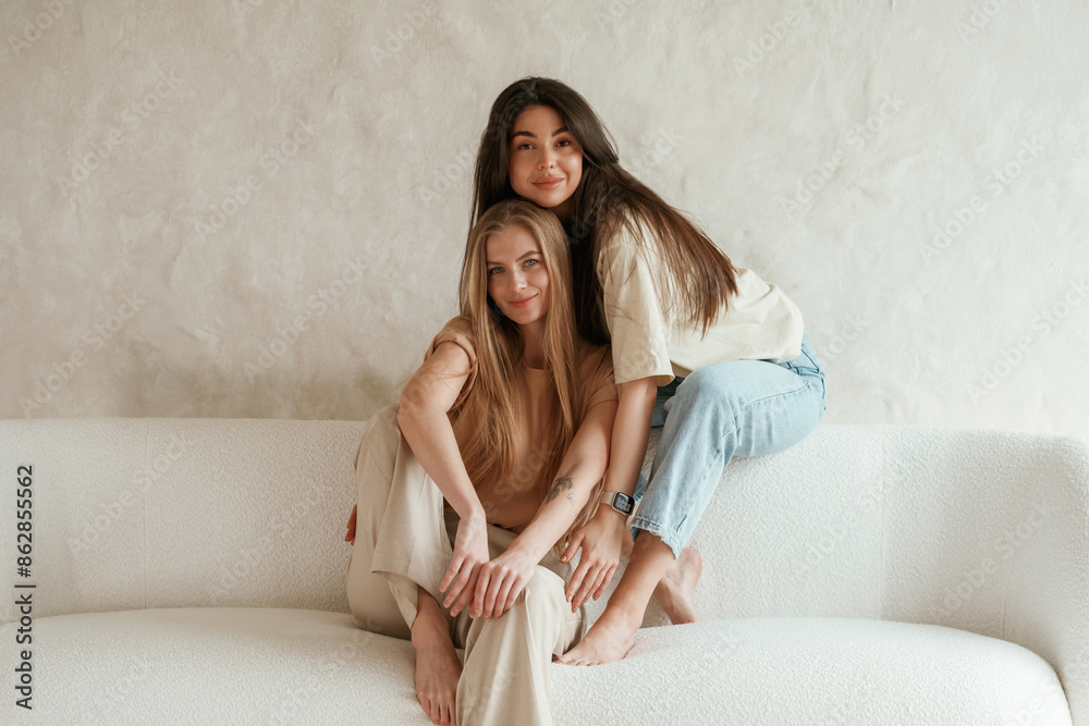 Front view, sitting. Two happy young female best friends are indoors Front view, sitting. Two happy young female best friends are indoors