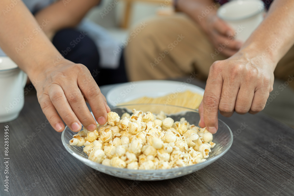 Selective focus, Hands of human picking up popcorn in plate on table during meeting with friends and enjoy eating together Selective focus, Hands of human picking up popcorn in plate on table during meeting with friends and enjoy eating together