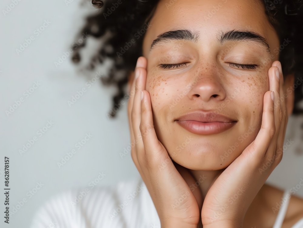 Young woman with curly hair and freckles smiling and touching her face with closed eyes, enjoying a moment of peace and relaxation. Young woman with curly hair and freckles smiling and touching her face with closed eyes, enjoying a moment of peace and relaxation.