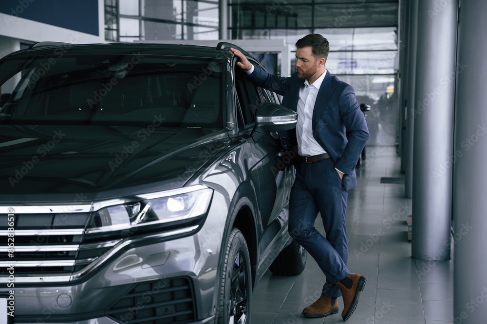 Looking at the automobile. A businessman is in a car dealership Looking at the automobile. A businessman is in a car dealership