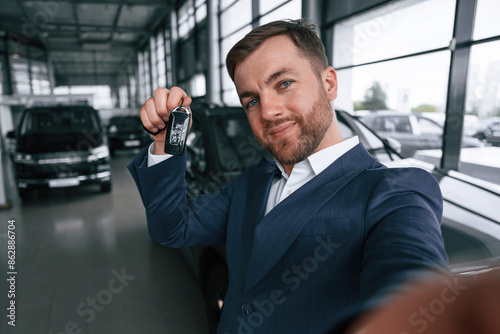 Making a selfie, with keys for new automobile. A businessman is in a car dealership © standret