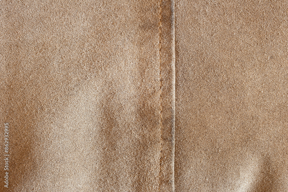 Fototapeta premium Close-up of a beige textured fabric with vertical seam, showcasing its fine, soft surface and precise seams, highlights the fabric’s luxurious texture and the natural color of the leather.