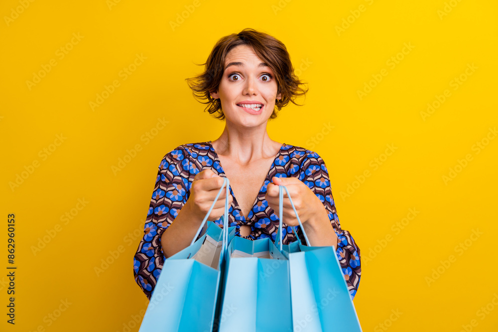 Photo of young funny girl nervous biting lips open her desirable shopping bags with different clothes isolated on yellow color background