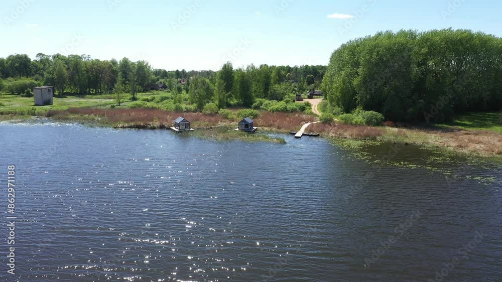 Aerial view of two small cabins on docks by a lake, surrounded by lush greenery and reeds. Clear sky and copy space. Aerial view of two small cabins on docks by a lake, surrounded by lush greenery and reeds. Clear sky and copy space.