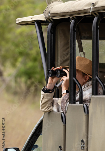 Canvas Print Woman in brown brimmed hat looks through binoculars from car, specialized open safari vehicle