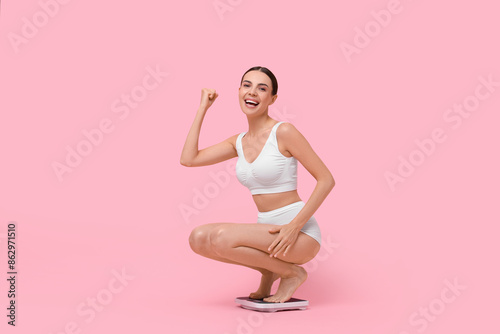 Diet and weight loss concept. Happy young woman on floor scale against pink background