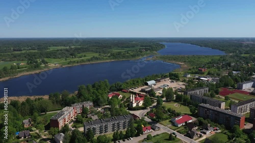 Balvi, Latvia - May 23, 2024 - Aerial view of a town near a large river, surrounded by lush greenery and a clear sky. Visible residential buildings and countryside. Copy space. photo