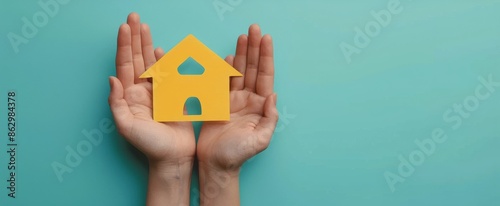 Hands Holding Paper House Cutout Against Blue Background