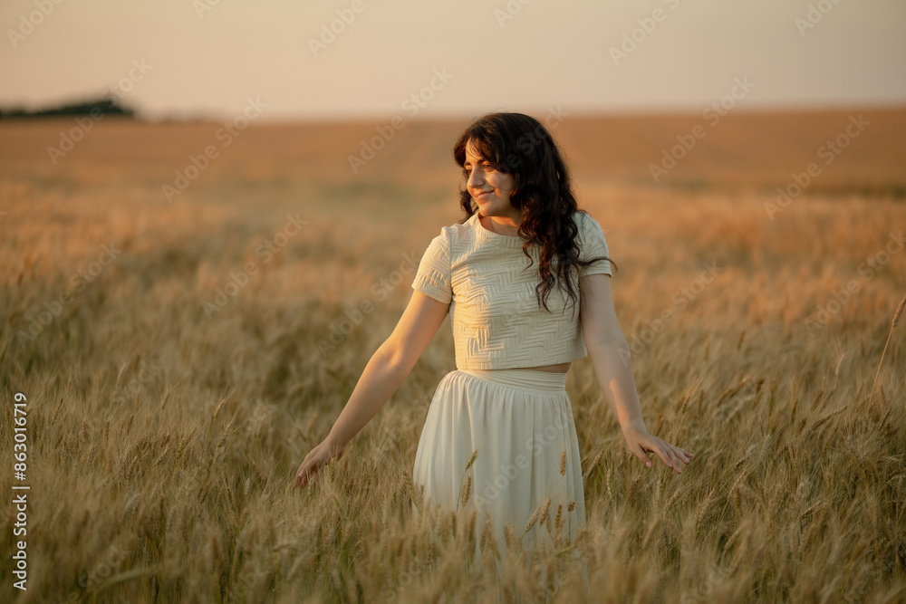 Obraz premium A young brunette walks in wheat fields at sunset in summer. Growing organic wheat and barley.
