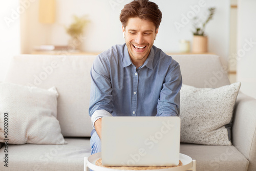 Remote Work Concept. Man Making Video Call Using Laptop Sitting On Couch At Home. Empty Space © Prostock-studio